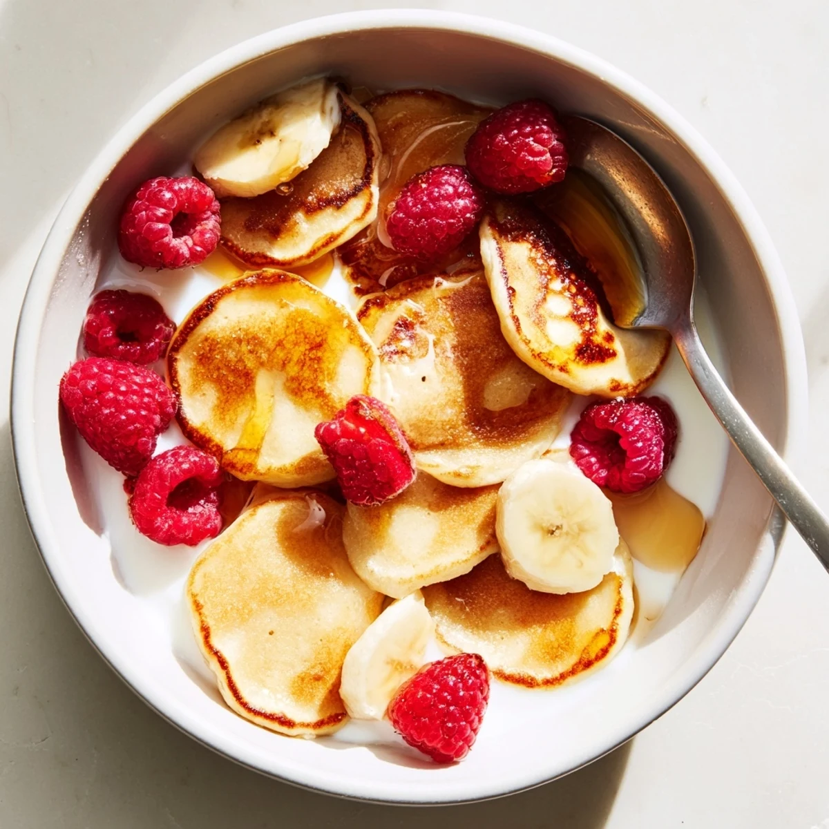Adorable mini pancake cereal served in a bowl with fresh berries and syrup.