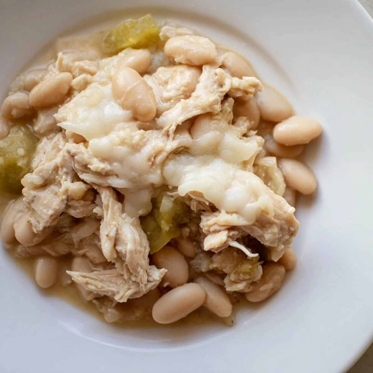 Steaming bowl of 35-Minute White Cheddar Apple Chicken Chili, topped with extra shredded cheese and fresh apple.