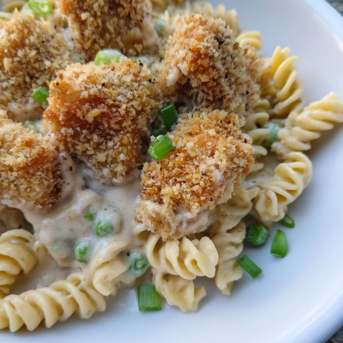 A bowl of Crispy Chicken Ranch Pasta Salad, featuring vibrant green peas and diced red peppers mixed into creamy ranch-coated rotini, topped with crunchy chicken pieces.
