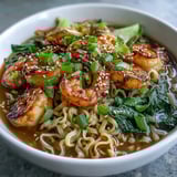 Sizzling Asian Noodle Bowl with Shrimp and Scallops garnished with sesame seeds, lime wedges, and fresh cilantro beside chopsticks.  