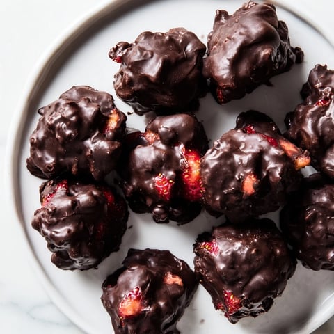 Frozen strawberry yogurt clusters, coated in dark chocolate, look sweet and refreshing.