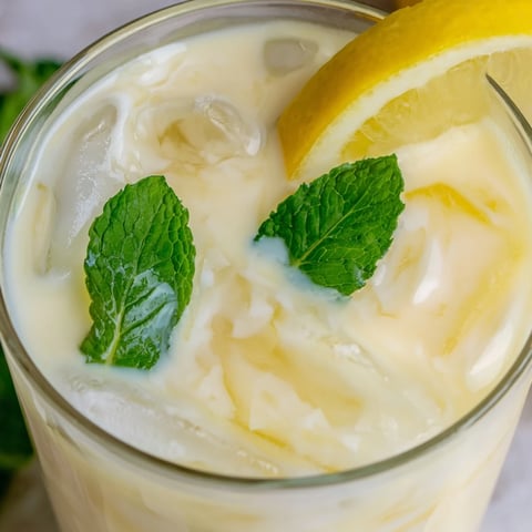 Creamy lemonade drink fills tall glasses with ice, garnished by lemon slices and fresh mint leaves.