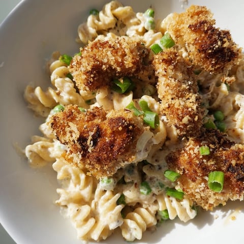 Tender pasta and golden-brown, crispy chicken bites tossed with sweet peas and bell peppers in a creamy ranch dressing, served in a white bowl.
