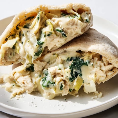 Golden-brown baked pita pockets stuffed with creamy spinach artichoke chicken and melted cheese, served on a rustic plate.  
