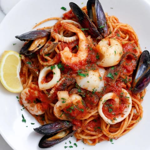A beautiful bowl with Seafood Marinara Pasta, garnished with fresh parsley and lemon wedges for serving.