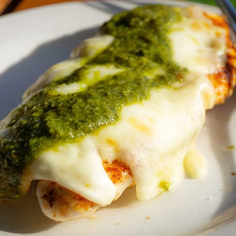 A close-up of a pesto chicken melt sandwich, featuring gooey cheese and fresh tomato slices.