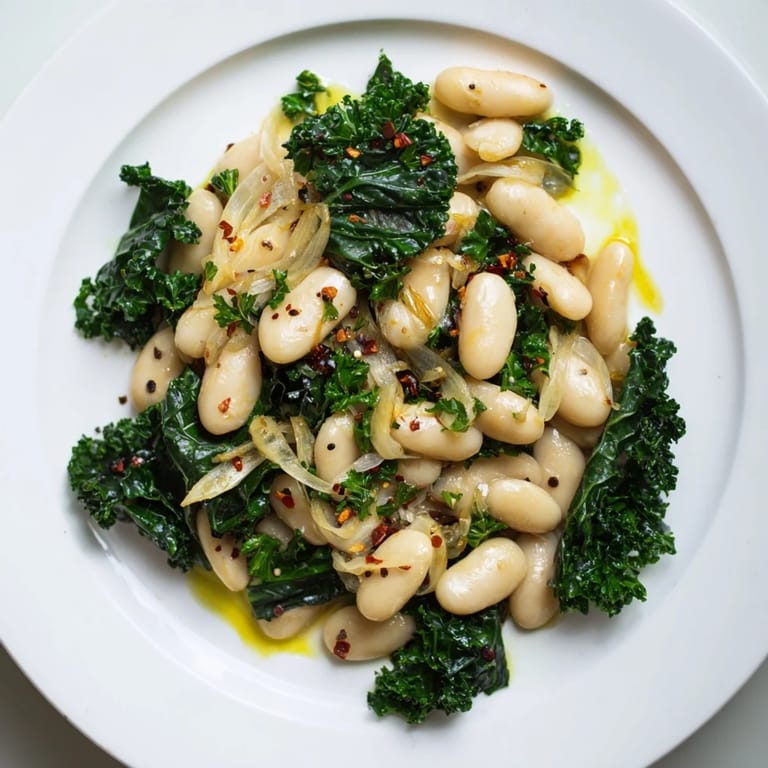 A bowl of vibrant garlicky beans with winter greens, drizzled with olive oil, ready to eat.